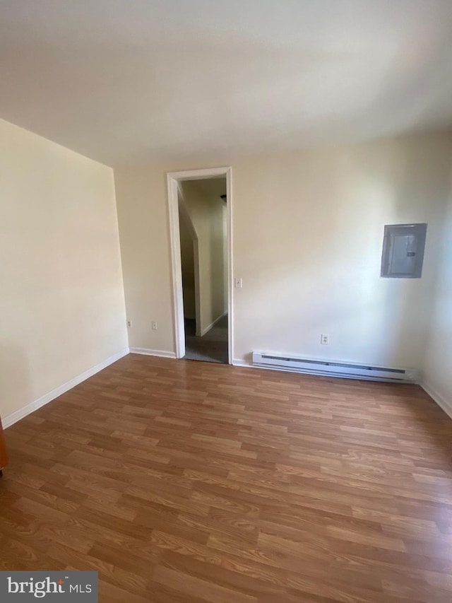 unfurnished room featuring a baseboard heating unit, electric panel, baseboards, and wood finished floors