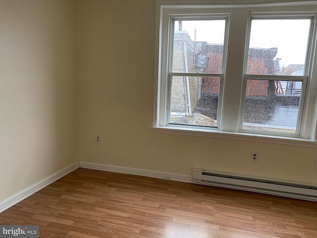 spare room featuring a baseboard heating unit, wood finished floors, and baseboards