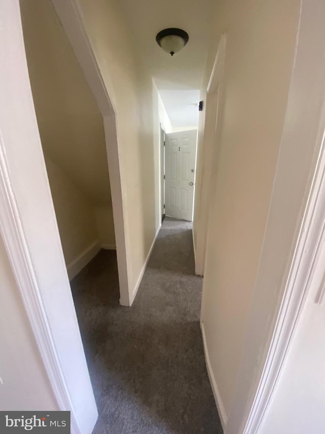 corridor with baseboards and dark carpet