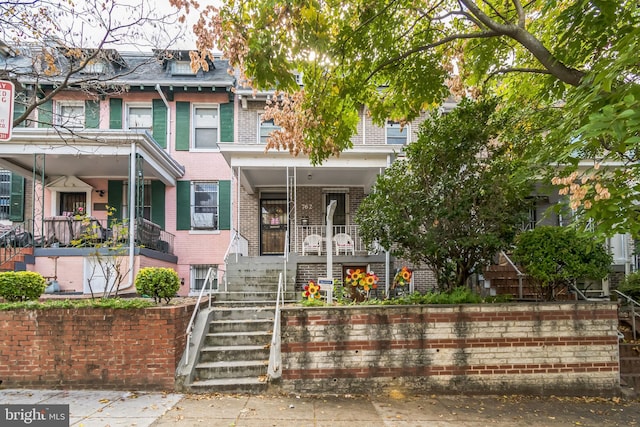 townhome / multi-family property with mansard roof, brick siding, a porch, and stairway