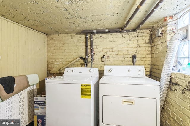 clothes washing area featuring brick wall and washer and clothes dryer