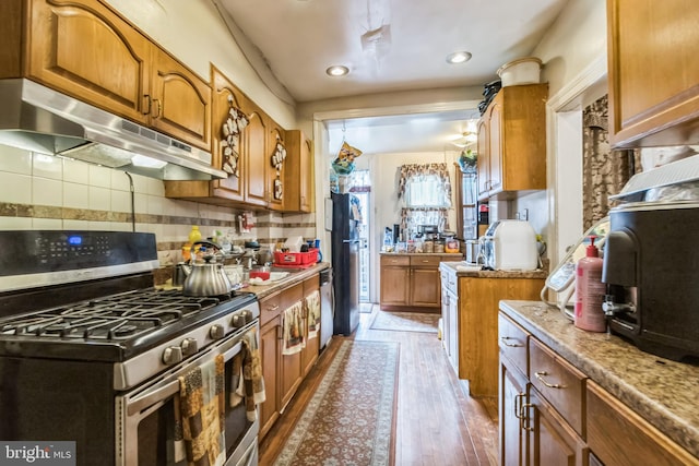 kitchen with under cabinet range hood, light wood finished floors, stainless steel appliances, and brown cabinetry