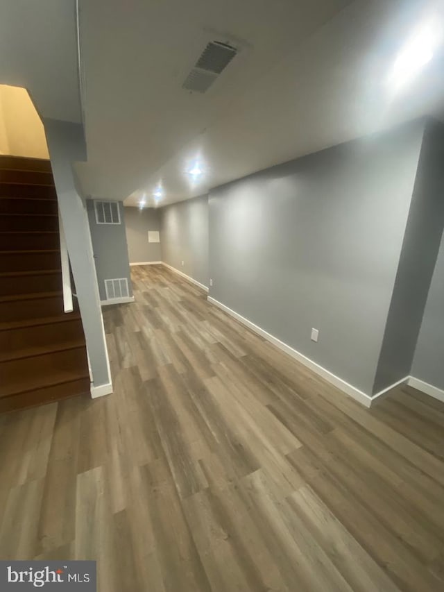 finished below grade area featuring baseboards, visible vents, stairway, and wood finished floors