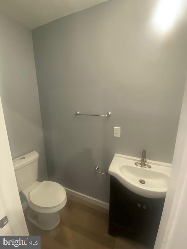 half bathroom featuring baseboards, vanity, toilet, and wood finished floors