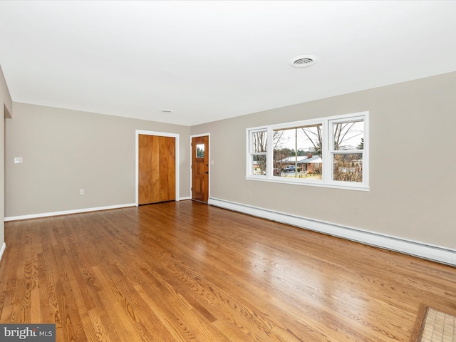 interior space featuring a baseboard heating unit, visible vents, baseboards, and wood finished floors