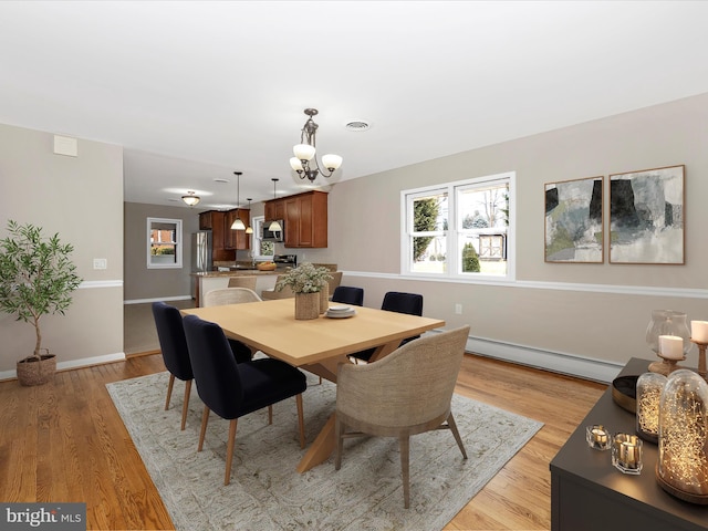 dining space featuring a chandelier, a baseboard radiator, visible vents, baseboards, and light wood-style floors