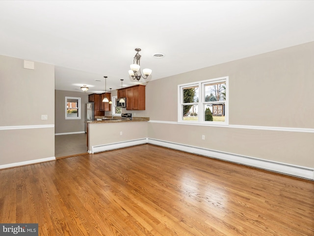 unfurnished living room featuring a healthy amount of sunlight, baseboard heating, and wood finished floors