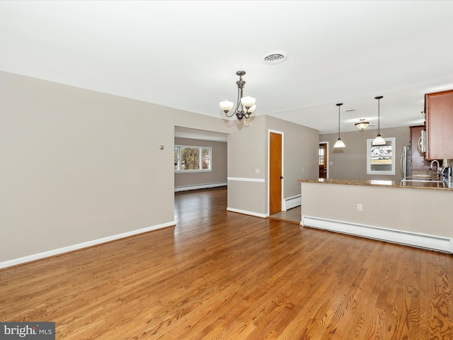 unfurnished living room featuring light wood-type flooring, a baseboard heating unit, baseboard heating, and a chandelier