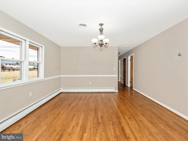 empty room with a notable chandelier, visible vents, baseboard heating, wood finished floors, and baseboards