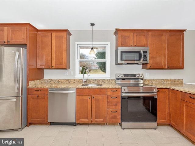 kitchen with stainless steel appliances, brown cabinets, a sink, and light stone counters