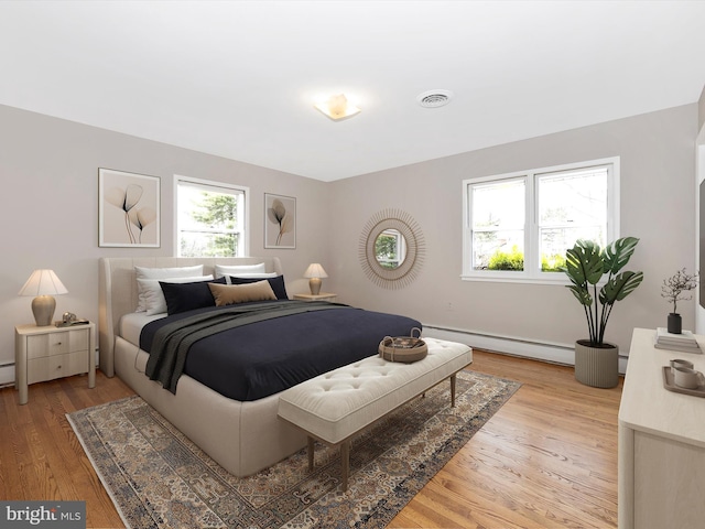 bedroom with a baseboard heating unit, light wood-type flooring, and visible vents