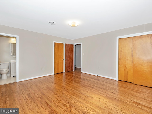 unfurnished bedroom featuring visible vents, ensuite bath, light wood-style flooring, and baseboards