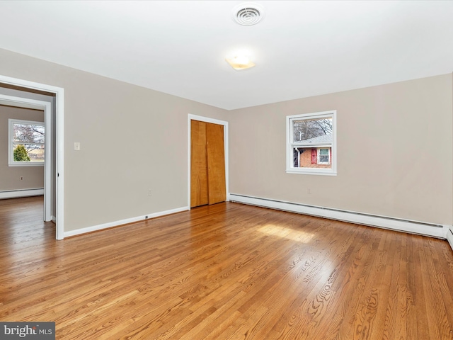 empty room with a baseboard heating unit, baseboards, visible vents, and light wood-style floors