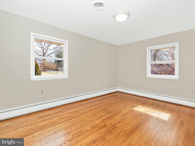 spare room with a baseboard radiator, visible vents, plenty of natural light, and wood finished floors