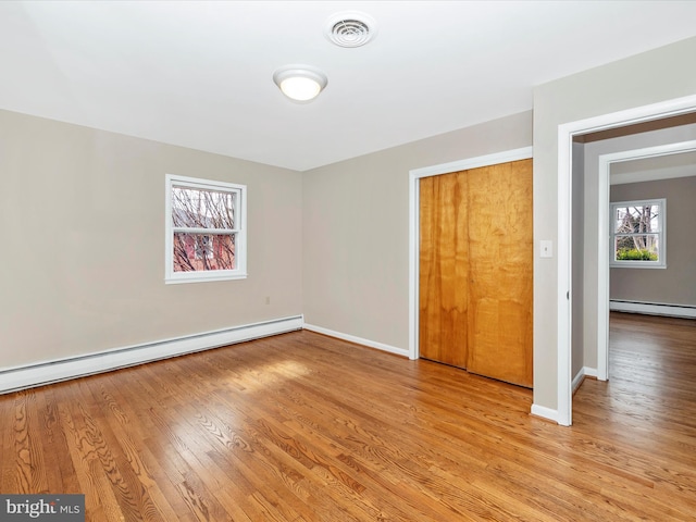 unfurnished bedroom featuring a baseboard radiator, a baseboard heating unit, visible vents, baseboards, and light wood finished floors