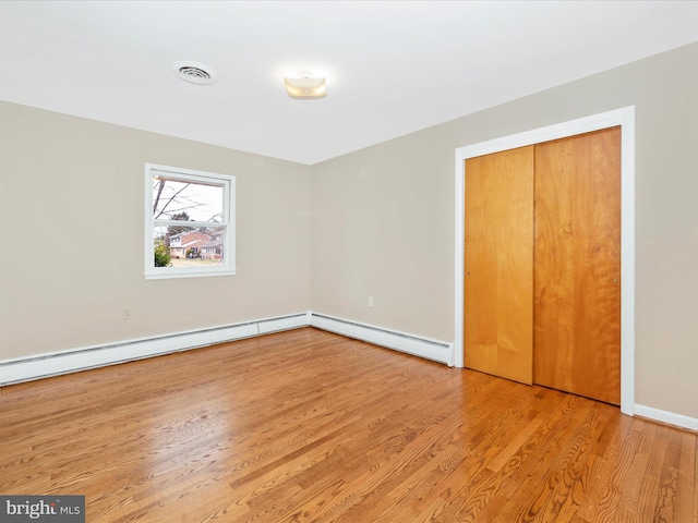 unfurnished bedroom featuring a baseboard heating unit, visible vents, baseboards, a closet, and light wood-type flooring