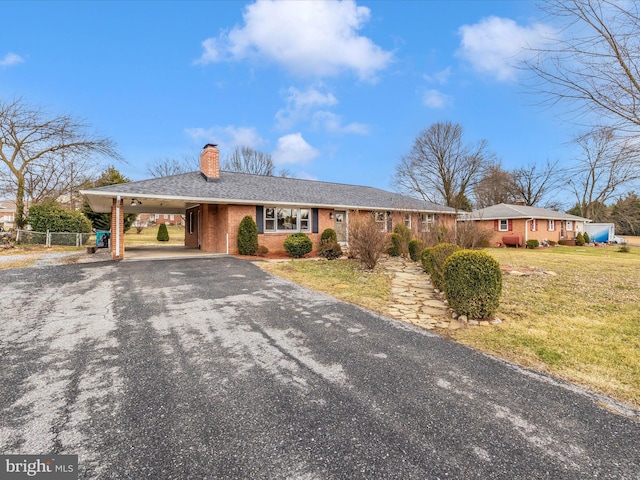 ranch-style home with aphalt driveway, brick siding, a chimney, a carport, and a front lawn