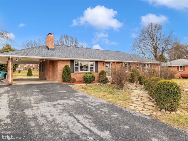 ranch-style house with brick siding, driveway, roof with shingles, a carport, and a chimney