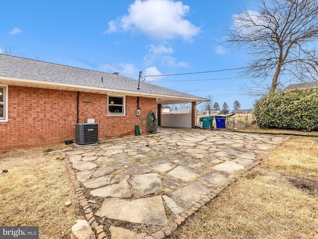 rear view of property featuring central AC unit, brick siding, driveway, roof with shingles, and a carport