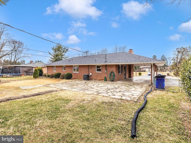 rear view of house with central air condition unit, a trampoline, a lawn, and a carport