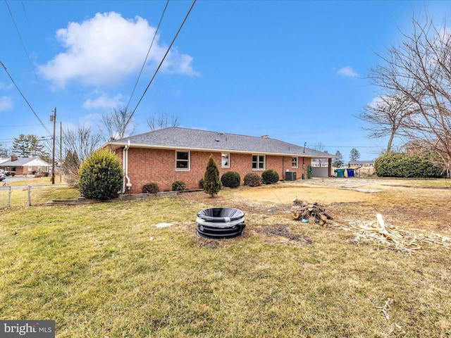 back of house featuring brick siding, a lawn, central AC unit, and fence