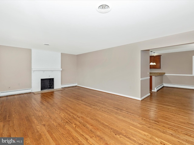 unfurnished living room with light wood-style flooring, baseboard heating, a brick fireplace, and visible vents