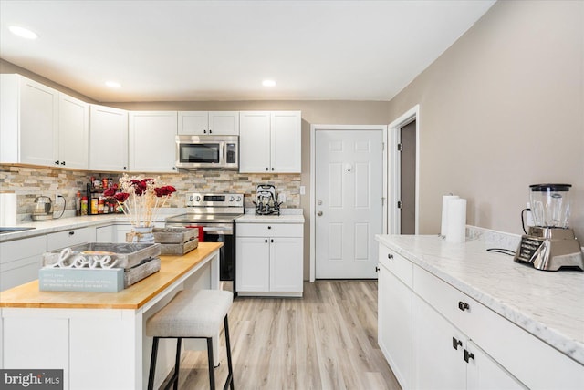 kitchen featuring butcher block countertops, white cabinetry, stainless steel appliances, and backsplash