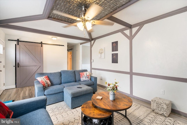 living area featuring a barn door, baseboards, ceiling fan, and wood finished floors