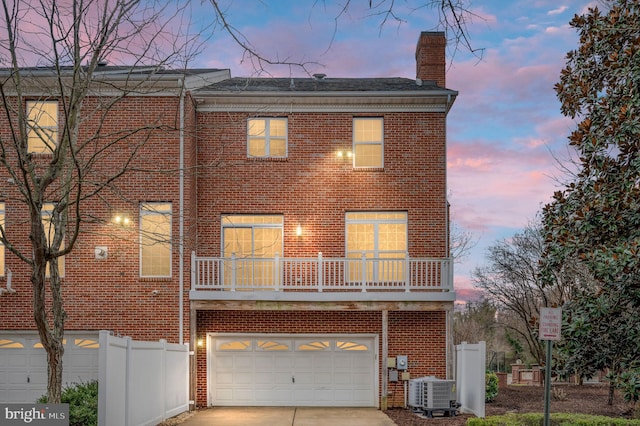 back of property at dusk featuring driveway, central air condition unit, a chimney, and brick siding