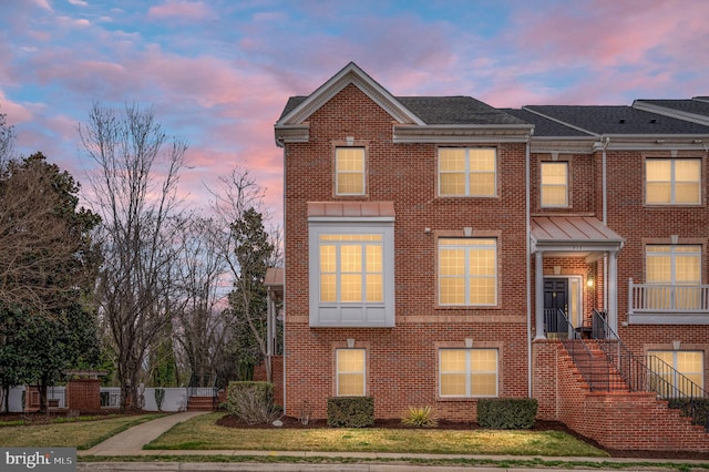 townhome / multi-family property featuring roof with shingles, a lawn, and brick siding