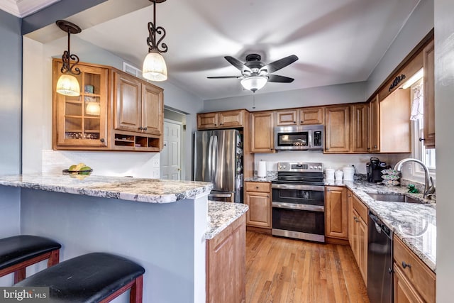 kitchen featuring a breakfast bar area, appliances with stainless steel finishes, a peninsula, light wood-type flooring, and a sink