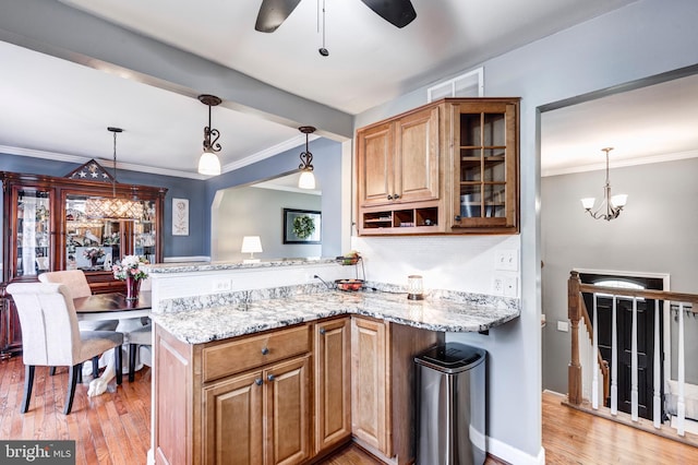 kitchen with hanging light fixtures, light wood finished floors, glass insert cabinets, and light stone countertops