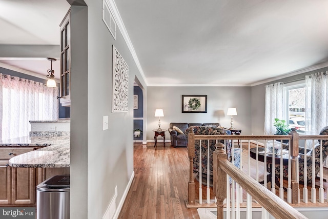 hallway featuring baseboards, wood finished floors, visible vents, and crown molding