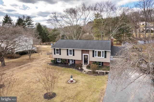 split foyer home with driveway, brick siding, a front lawn, and a chimney