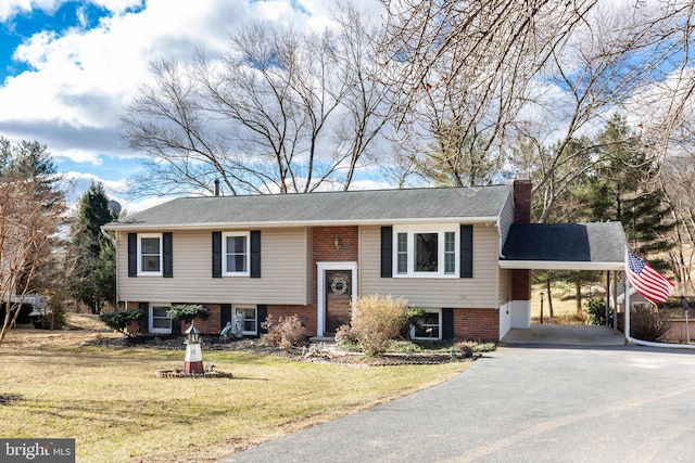 raised ranch with aphalt driveway, brick siding, a chimney, an attached carport, and a front lawn