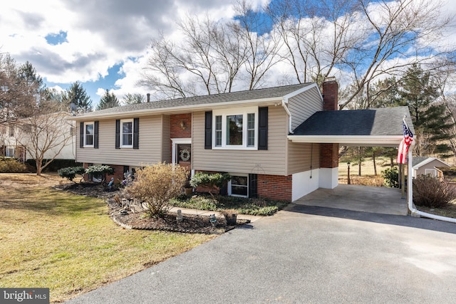 raised ranch featuring a carport, a chimney, a front lawn, and aphalt driveway