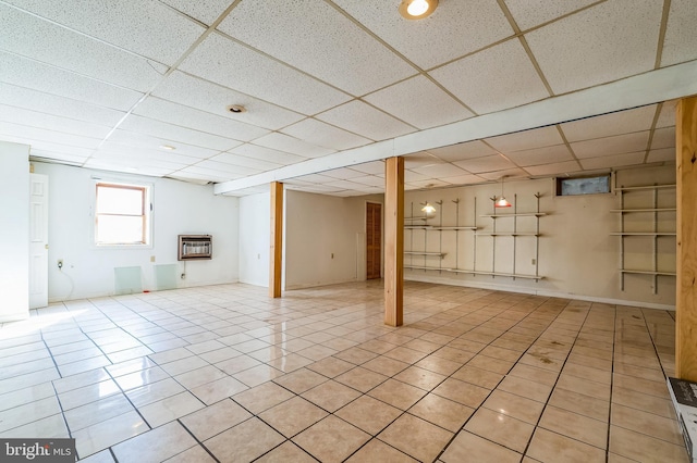 below grade area with a paneled ceiling, heating unit, baseboards, and light tile patterned flooring