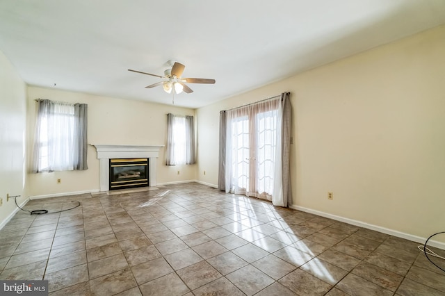 unfurnished living room with a glass covered fireplace, tile patterned floors, a ceiling fan, and baseboards