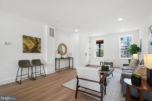 living room with recessed lighting, visible vents, baseboards, and wood finished floors