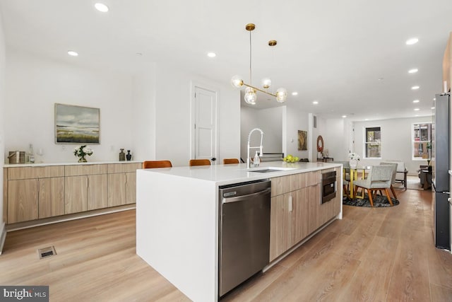 kitchen featuring a center island with sink, stainless steel appliances, light wood-type flooring, light brown cabinets, and a sink