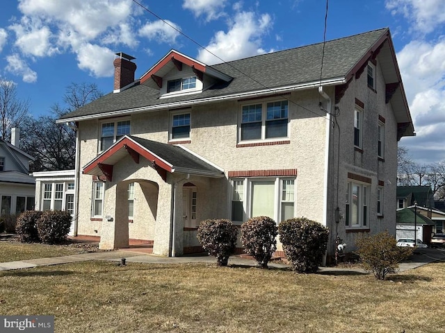 american foursquare style home featuring roof with shingles, a chimney, a front lawn, and stucco siding