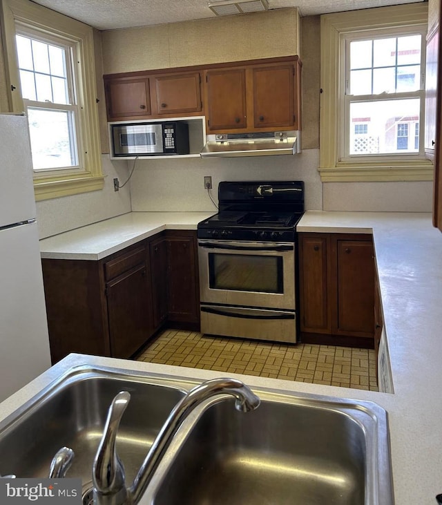 kitchen featuring stainless steel appliances, a textured ceiling, light countertops, under cabinet range hood, and a sink