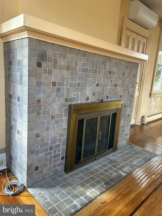 interior details featuring a baseboard heating unit, wood finished floors, an AC wall unit, and a glass covered fireplace