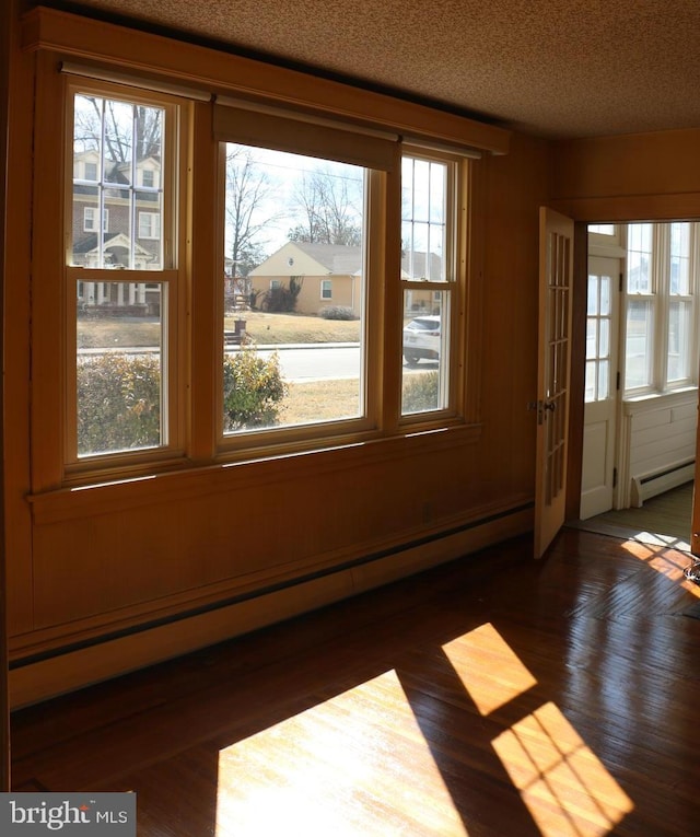 interior space with a textured ceiling, baseboard heating, a baseboard radiator, and a healthy amount of sunlight