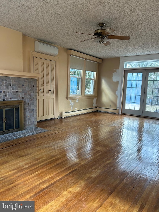 unfurnished living room featuring a brick fireplace, wood-type flooring, a textured ceiling, and an AC wall unit