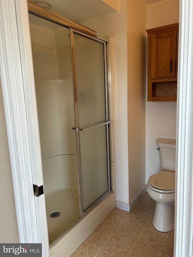 bathroom featuring toilet, a shower stall, baseboards, and tile patterned floors