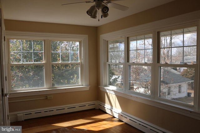 unfurnished sunroom featuring a baseboard heating unit, ceiling fan, and plenty of natural light