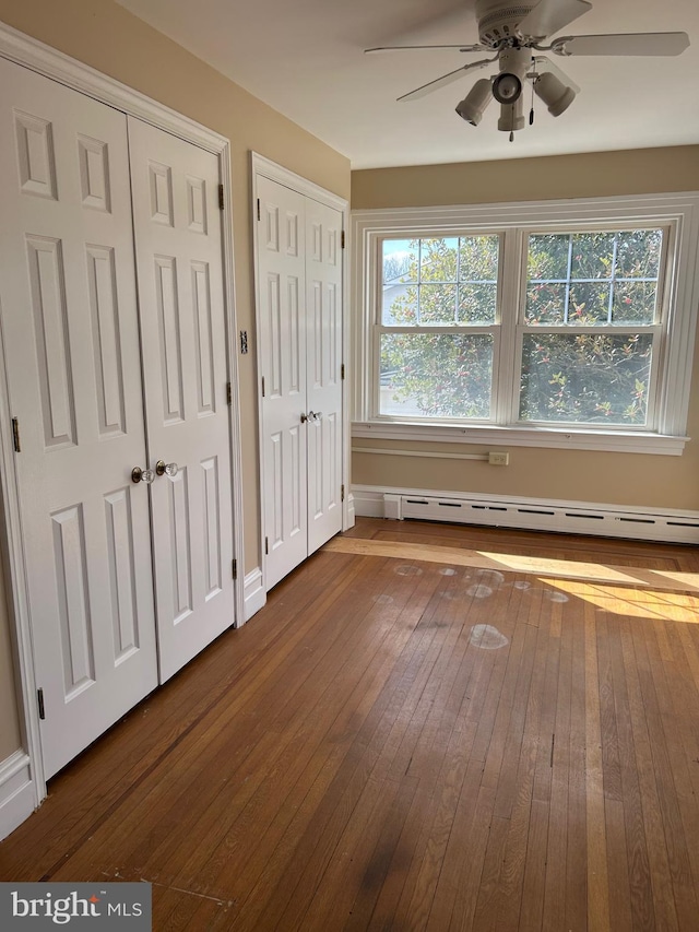 unfurnished bedroom featuring dark wood-type flooring, a baseboard radiator, multiple windows, and multiple closets