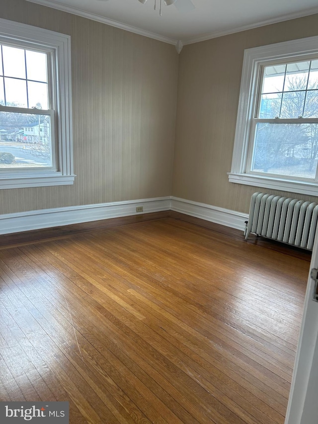 empty room with ceiling fan, baseboards, radiator, hardwood / wood-style floors, and crown molding