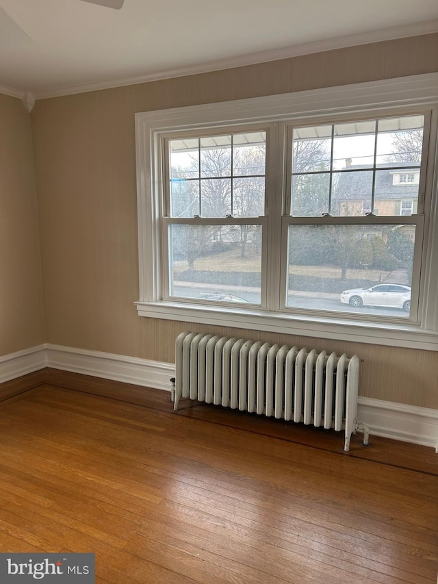 unfurnished room featuring radiator, a wealth of natural light, ornamental molding, and hardwood / wood-style floors